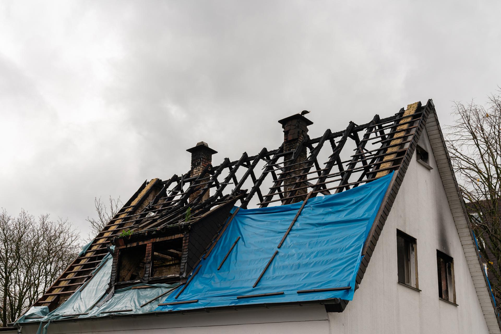 Fire damage visible on residential roof covered with blue tarp.